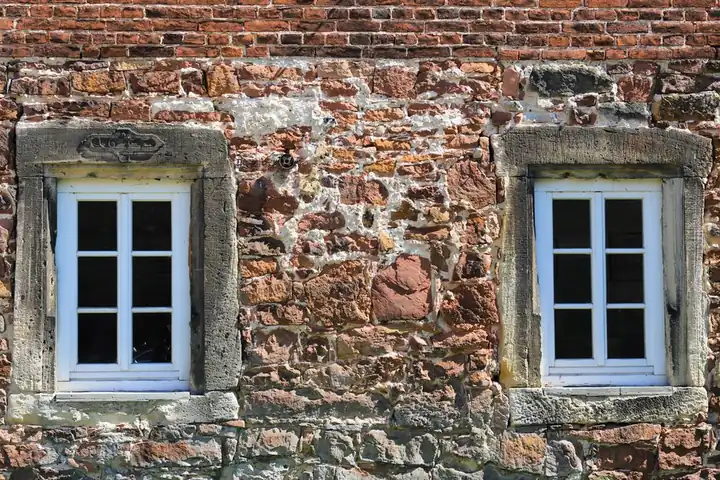 Close-up of a historic stone building facade featuring two symmetrical white-framed windows.