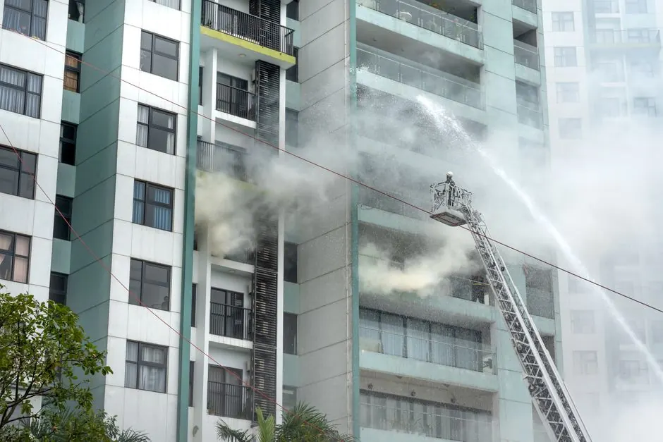 Firefighters on a ladder battling a fire in an urban residential high-rise.